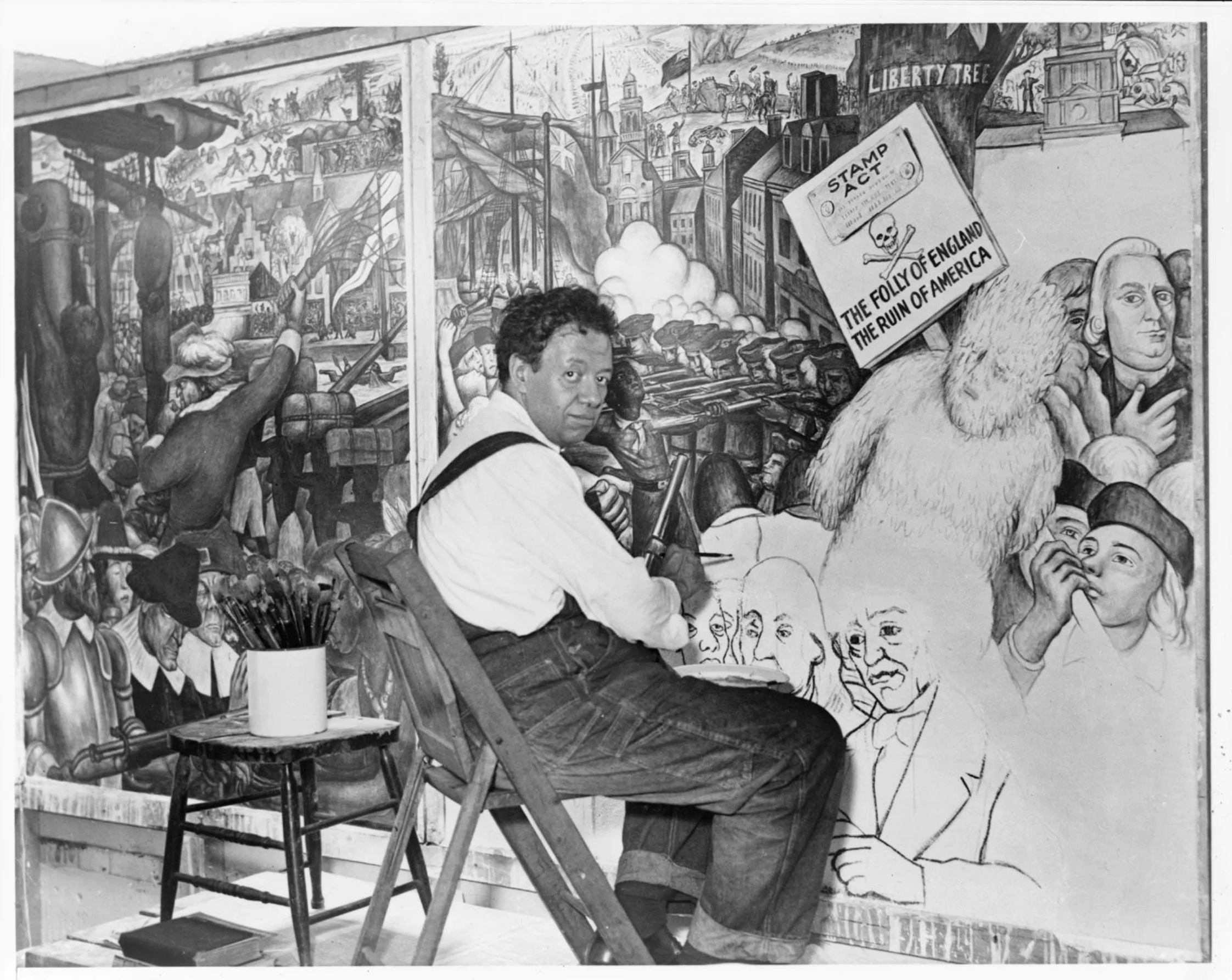 Diego Rivera, seated in front of a mural depicting the American